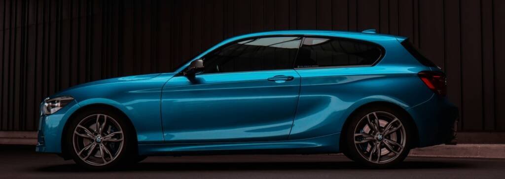 Blue BMW hatchback parked beside a wood-slat wall