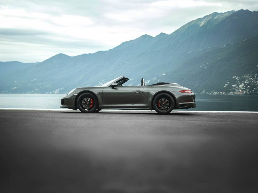 Silver convertible sports car parked lakeside with mountains behind